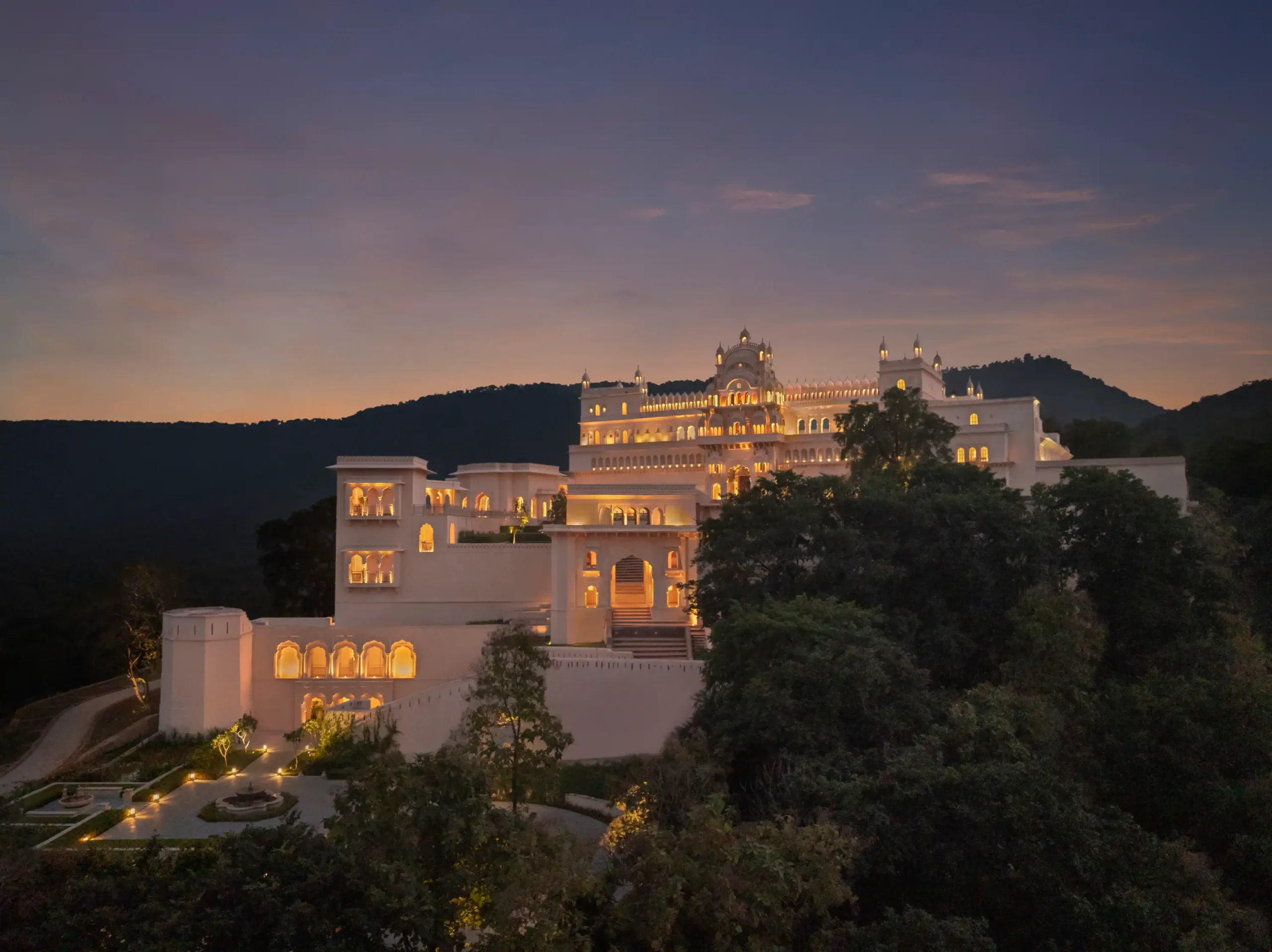 The Oberoi Rajgarh Palace illuminated at dusk, surrounded by forest